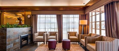 A lobby with a fireplace, striped sofas, a patterned rug, and a large window with curtains.