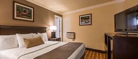 Habitación de hotel con una cama grande, televisión, escritorio y aire acondicionado instalado en la pared.