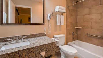 Un baño con lavamanos de encimera de granito, inodoro, bañera y toallero con toallas.