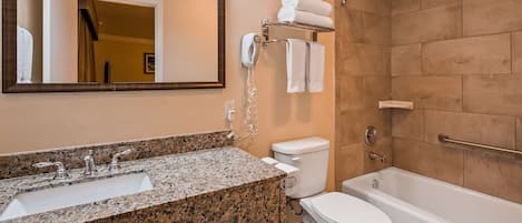 A bathroom with a granite countertop sink, a toilet, a bathtub, and a towel rack with towels.