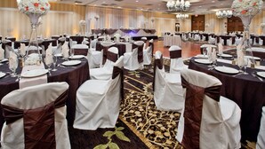 A banquet hall with round tables set for a formal event, featuring white and brown tablecloths, chairs with white and brown sashes, and floral centerpieces.