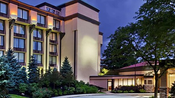 A multi-story hotel with a modern design, featuring a well-maintained garden and a parking area.