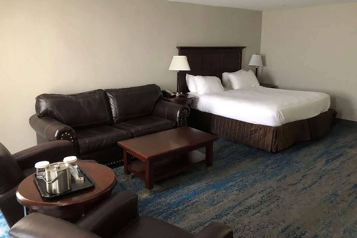 Habitación de hotel con cama, sofá de cuero, una mesita de centro y una pequeña mesa con bandeja.
