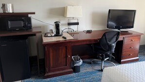 A hotel room with a wooden desk, a microwave, a coffee maker, a television, and a small trash bin.