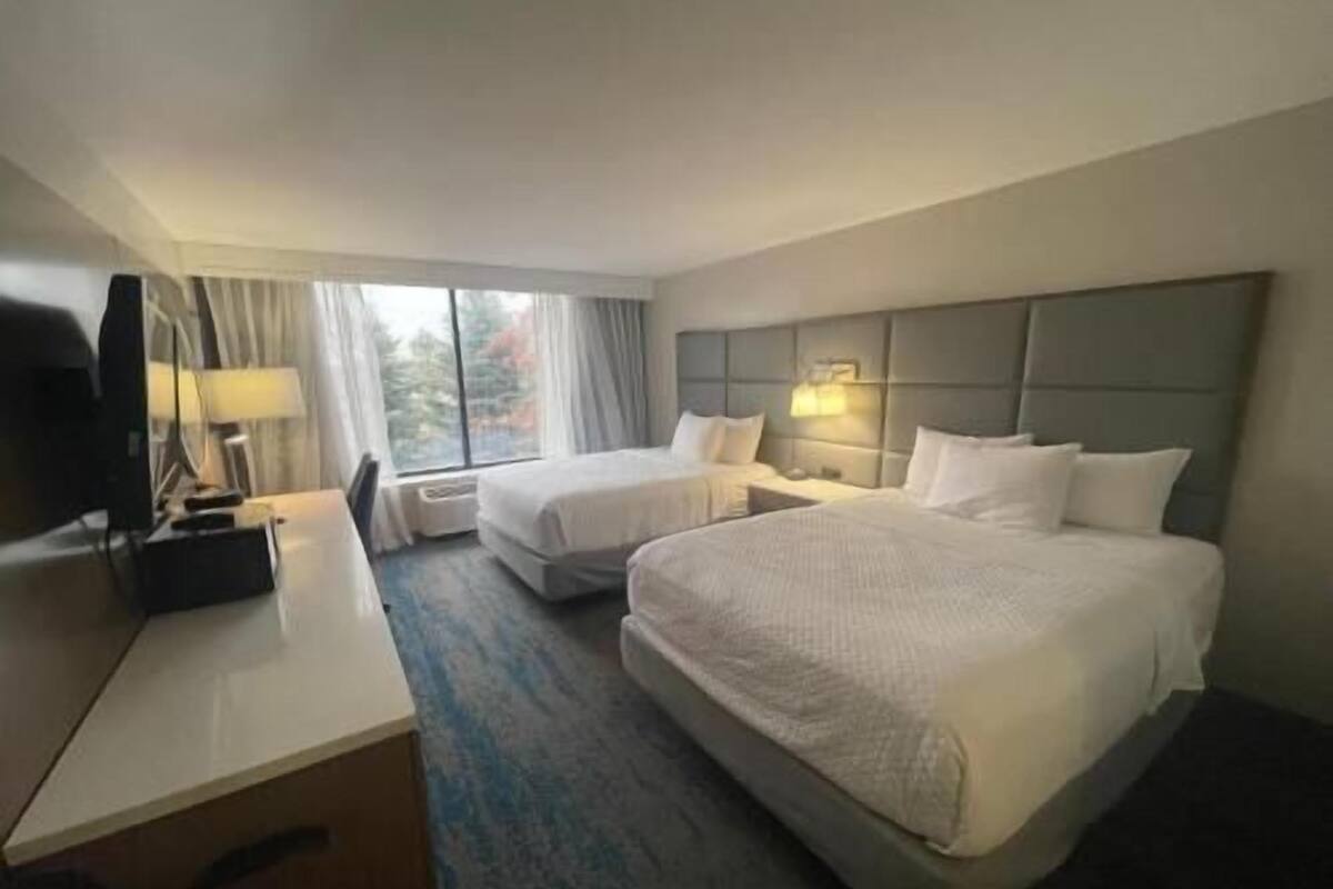 Una habitación de hotel con dos camas, un escritorio, un televisor y una ventana con cortinas.