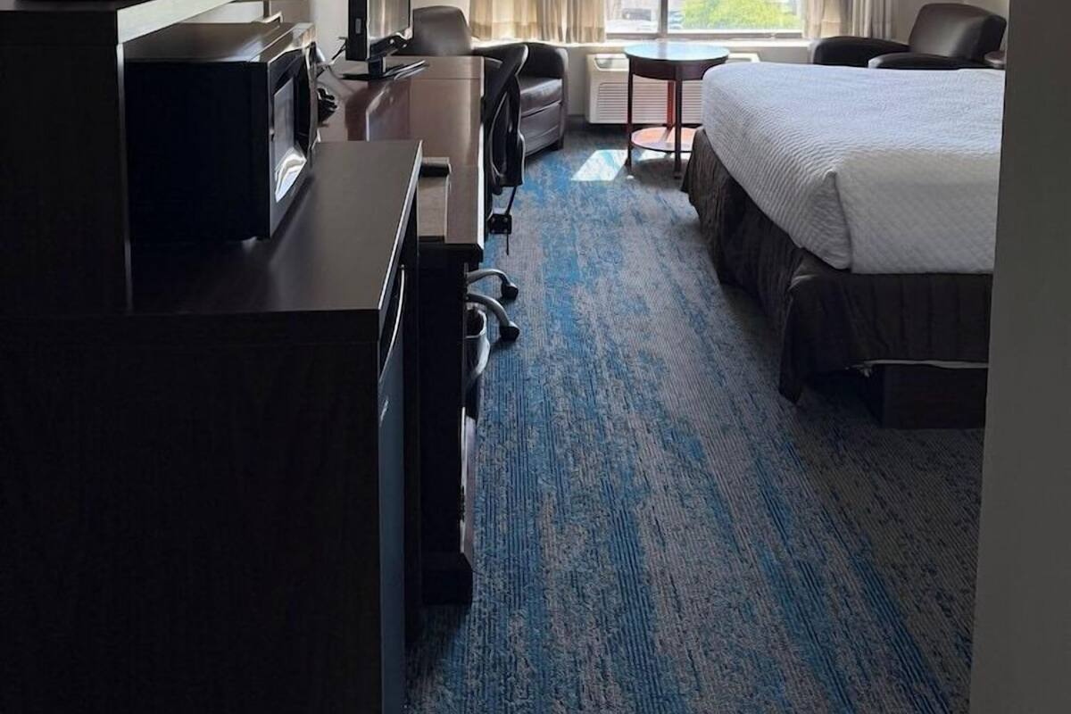A hotel room with a bed, desk, chair, and a view of greenery through the window.