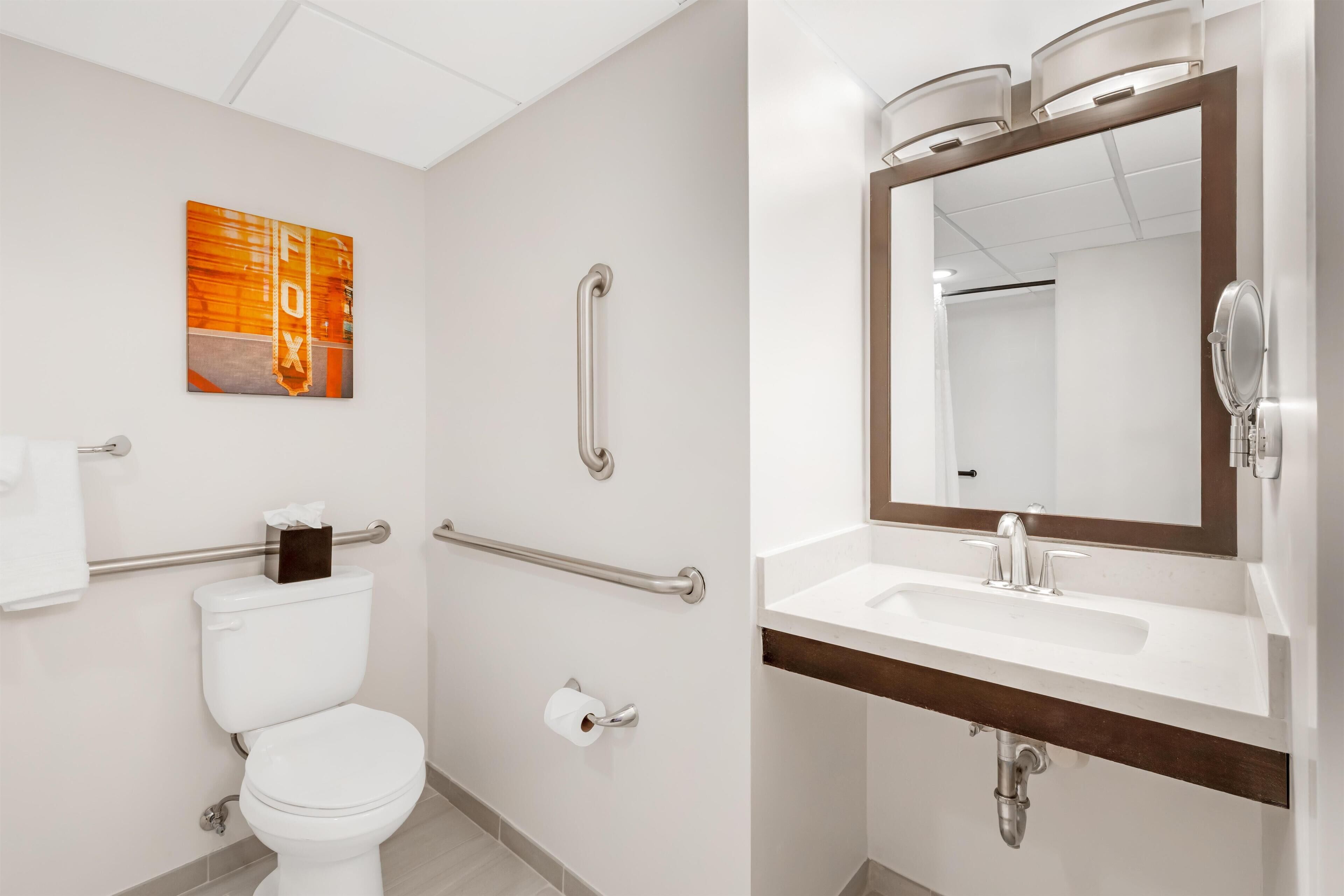 A modern bathroom with a toilet, handrails, a sink with a mirror, and a towel rack.
