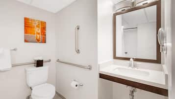 Une salle de bain moderne équipée de toilettes, de barres d’appui, d’un lavabo avec un miroir et d’un porte-serviettes.