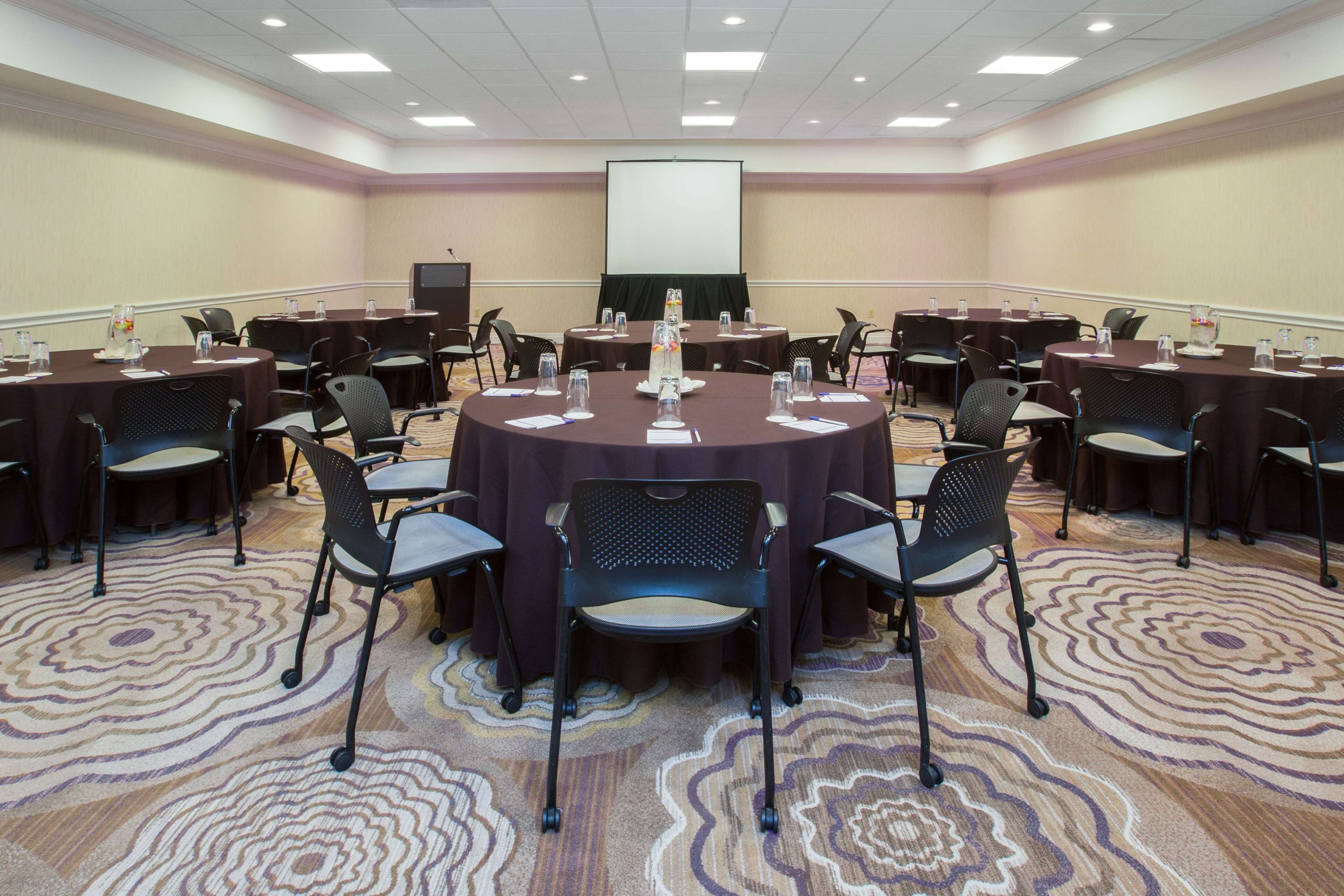 A conference room with round tables, chairs, and a projector screen.