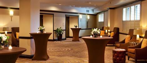 Un hall d’hôtel avec des tables rondes, des sièges confortables et un tapis à motifs.