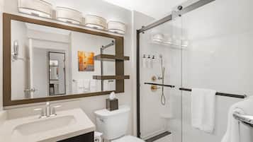 Un baño moderno con un espejo grande, un lavabo, un inodoro y una zona de ducha con mampara de vidrio.