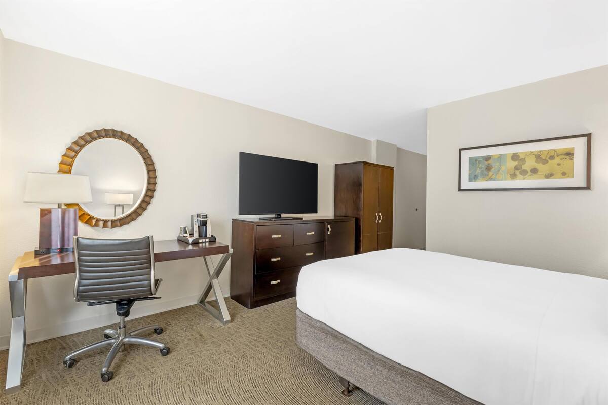 Une chambre d’hôtel équipée d’un lit, d’un bureau, d’une chaise, d’une télévision, d’une armoire et d’œuvres d’art accrochées au mur.