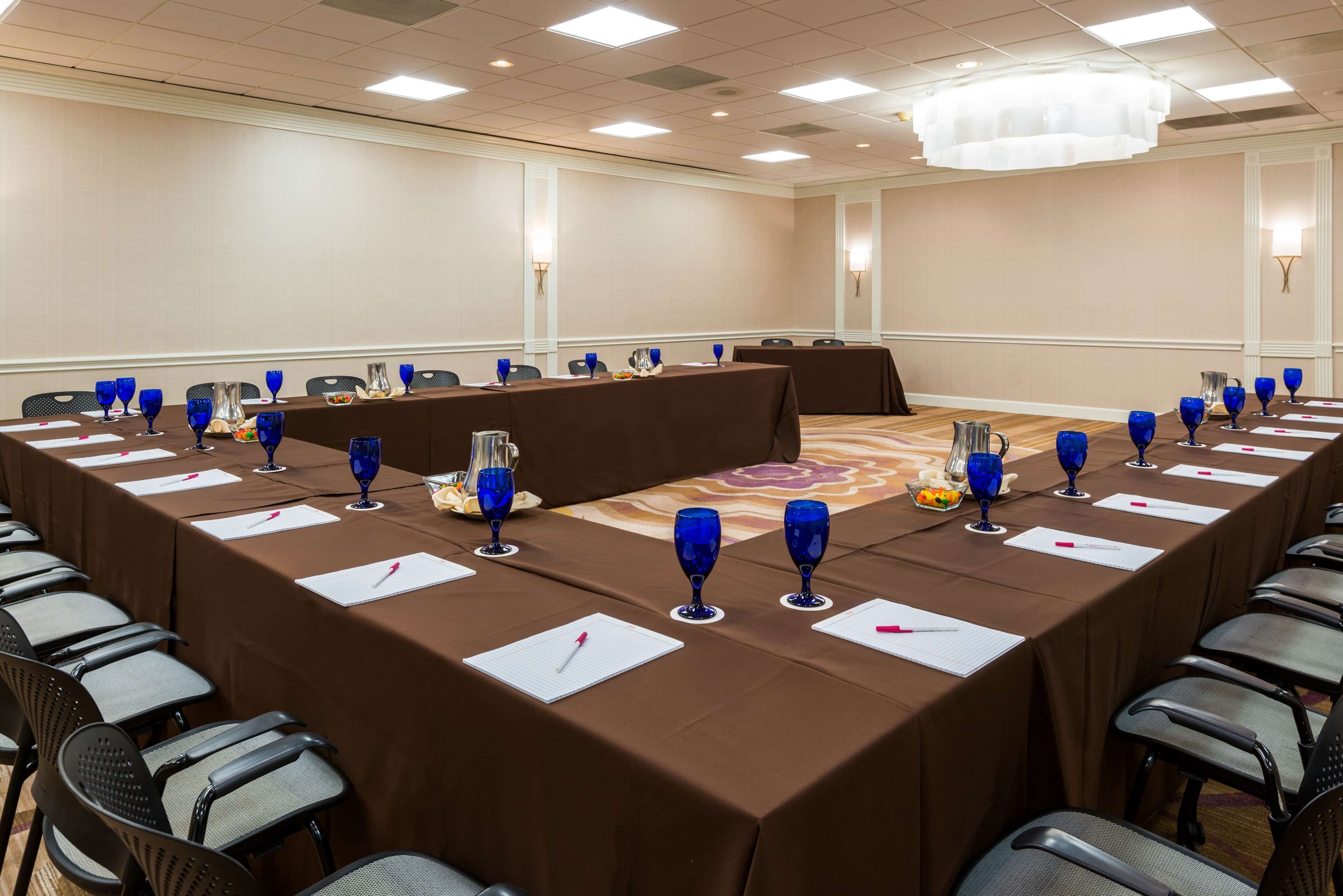 Un salón de conferencias con una larga mesa, cristalería azul y servilletas blancas.