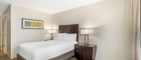 A hotel room with a large bed, two bedside lamps, a framed picture on the wall, and a carpeted floor.