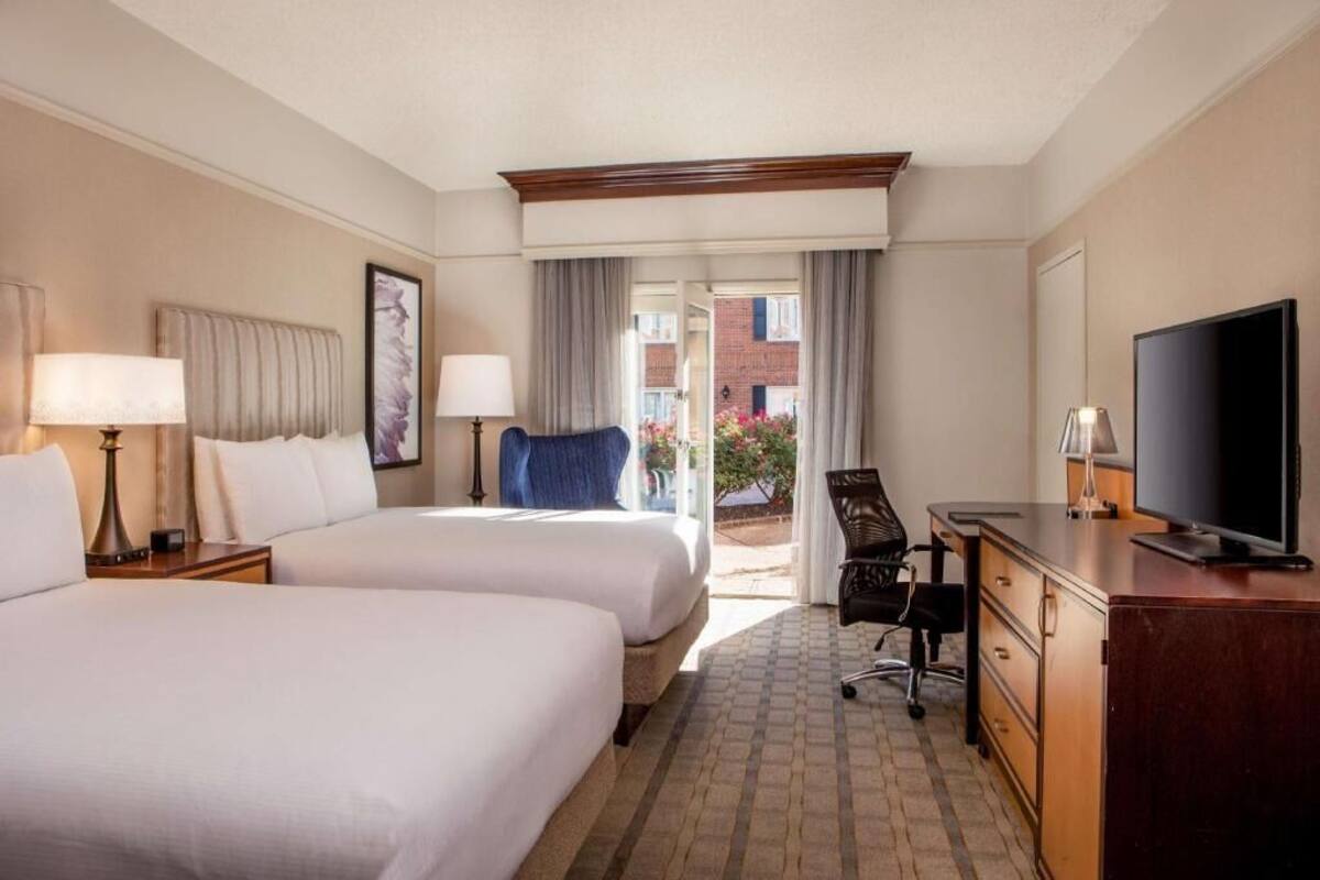 Een hotelkamer met twee bedden, een bureau, een stoel, een televisie en uitzicht buiten.