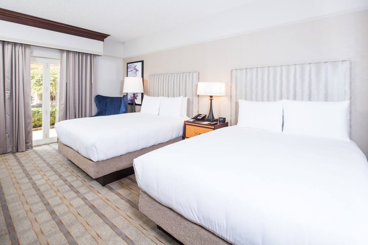 Een hotelkamer met twee bedden, een nachtkastje met een lamp, en uitzicht op het omliggende landschap via een schuifdeur.