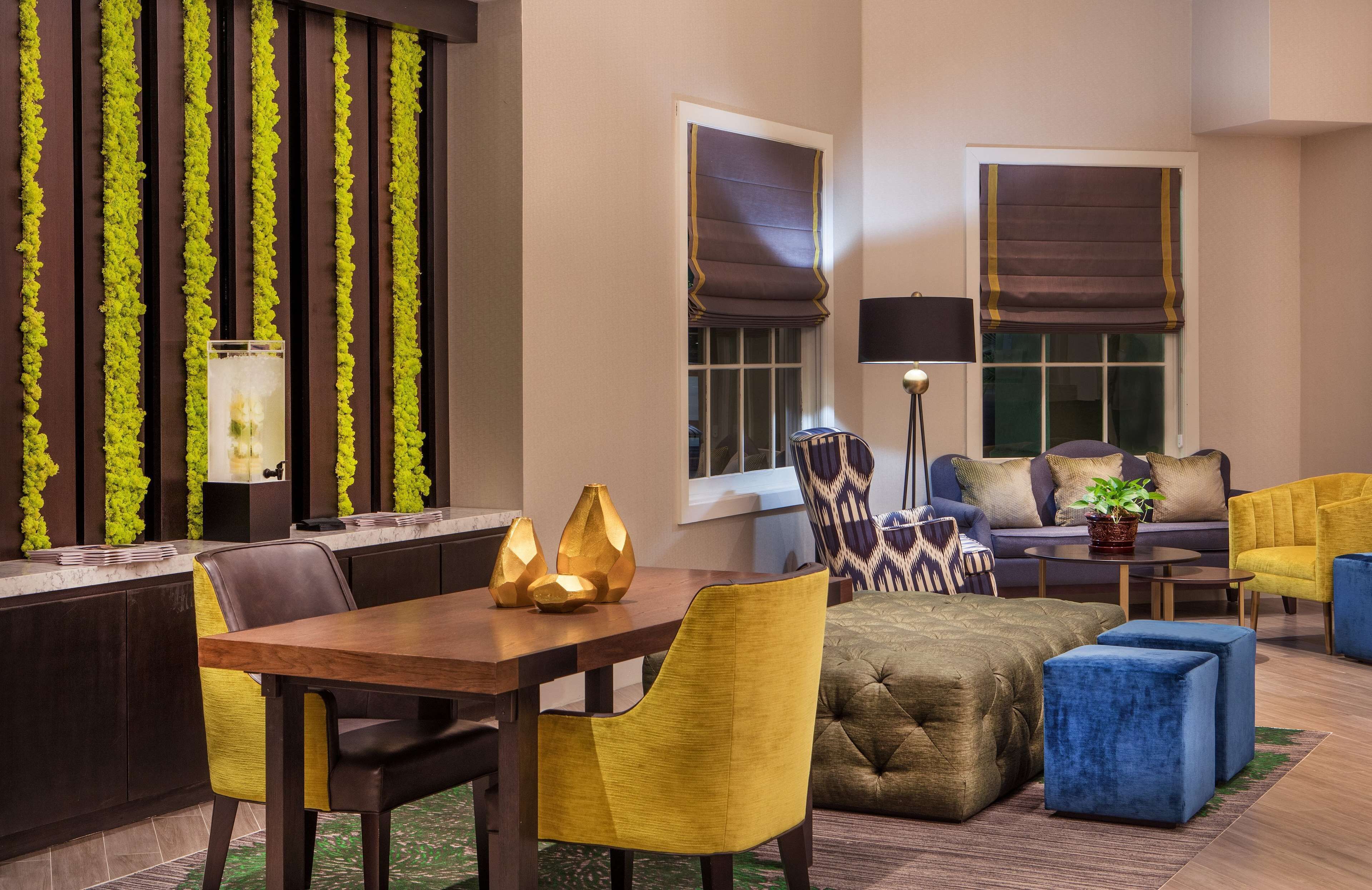 A modern hotel lobby with a dining area, sofas, and a large window with blinds.