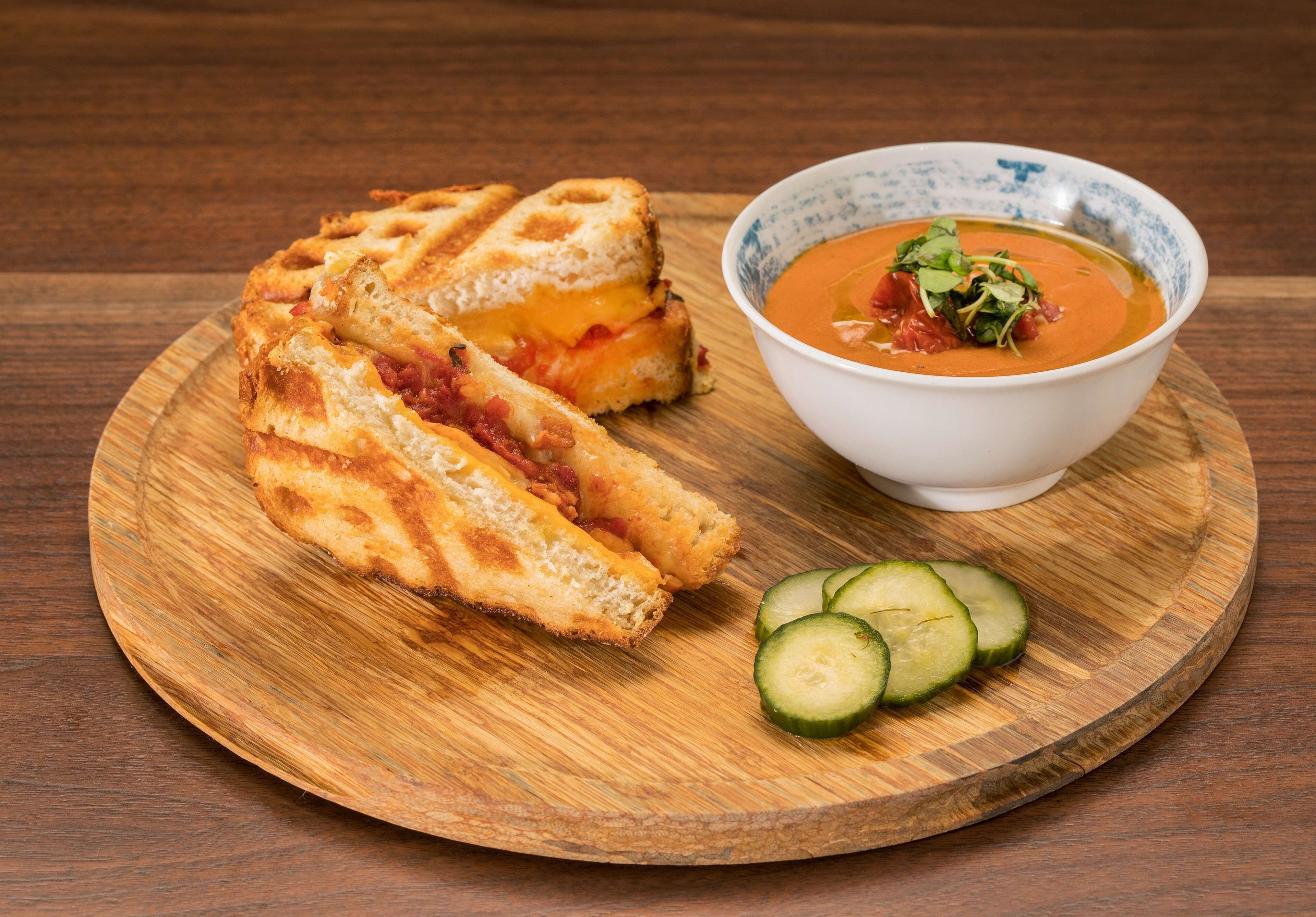 A grilled cheese sandwich and a bowl of soup on a wooden plate.