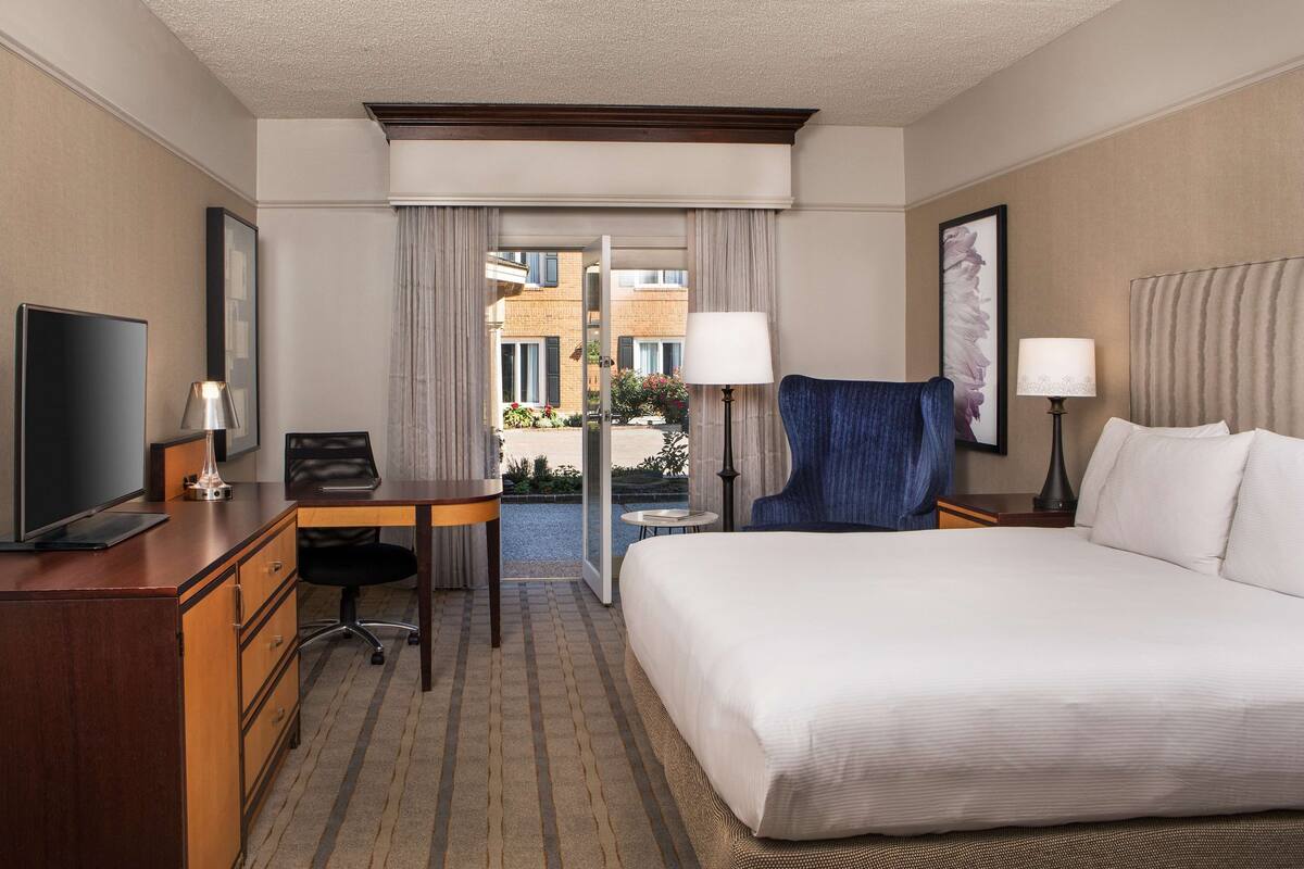 Een hotelkamer met een bed, een bureau, een stoel, een televisie en een raam met gordijnen.