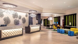 Eine moderne Hotelhalle mit Empfangstresen, Sitzgelegenheiten und dekorativen Wandbildern.