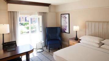 Une chambre d’hôtel comprenant un lit, deux tables de chevet avec des lampes, une chaise, une petite table ronde et une fenêtre avec des rideaux.