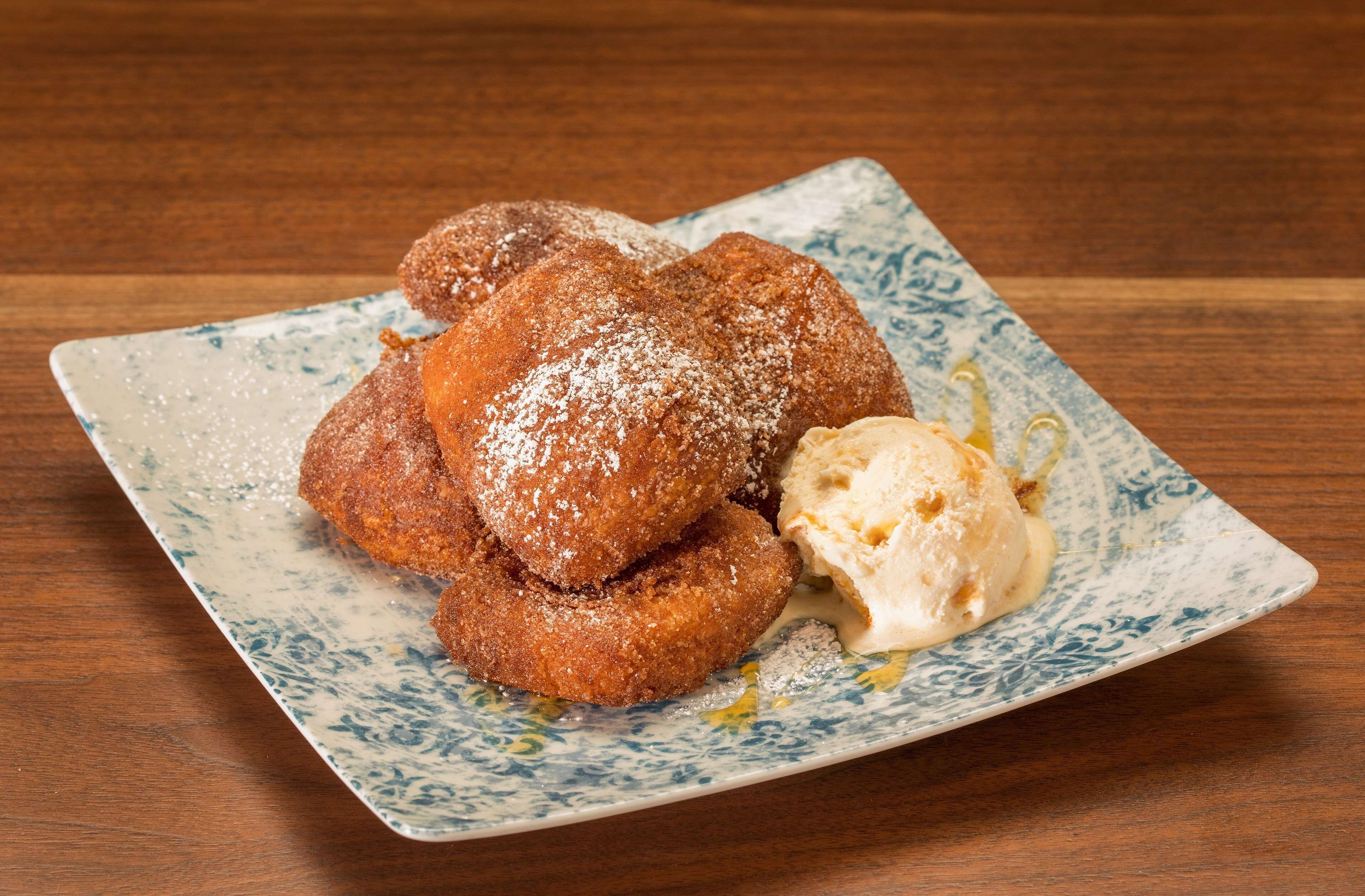 A plate of fried doughnuts with powdered sugar and a scoop of vanilla ice cream.