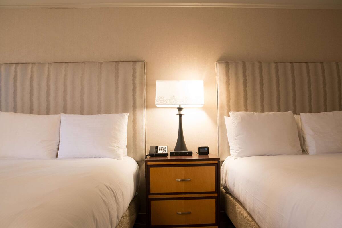 Een hotelkamer met twee bedden, een nachtkastje met een lamp, een klok en een telefoon.