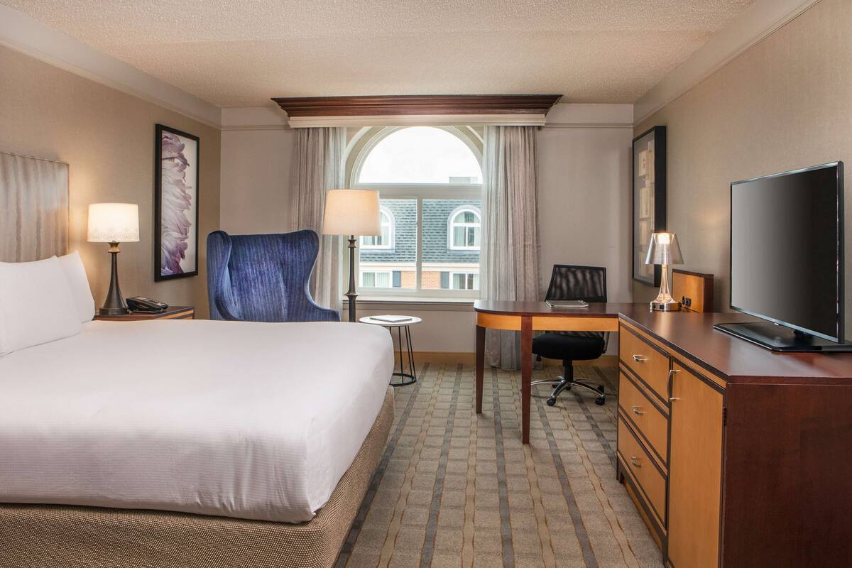 Hotelkamer met een groot bed, een bureau, een stoel, een televisie en een raam met uitzicht op gebouwen.