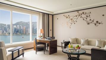 A hotel room with a city view, a desk with a laptop, a sofa, and a coffee table with fruit.