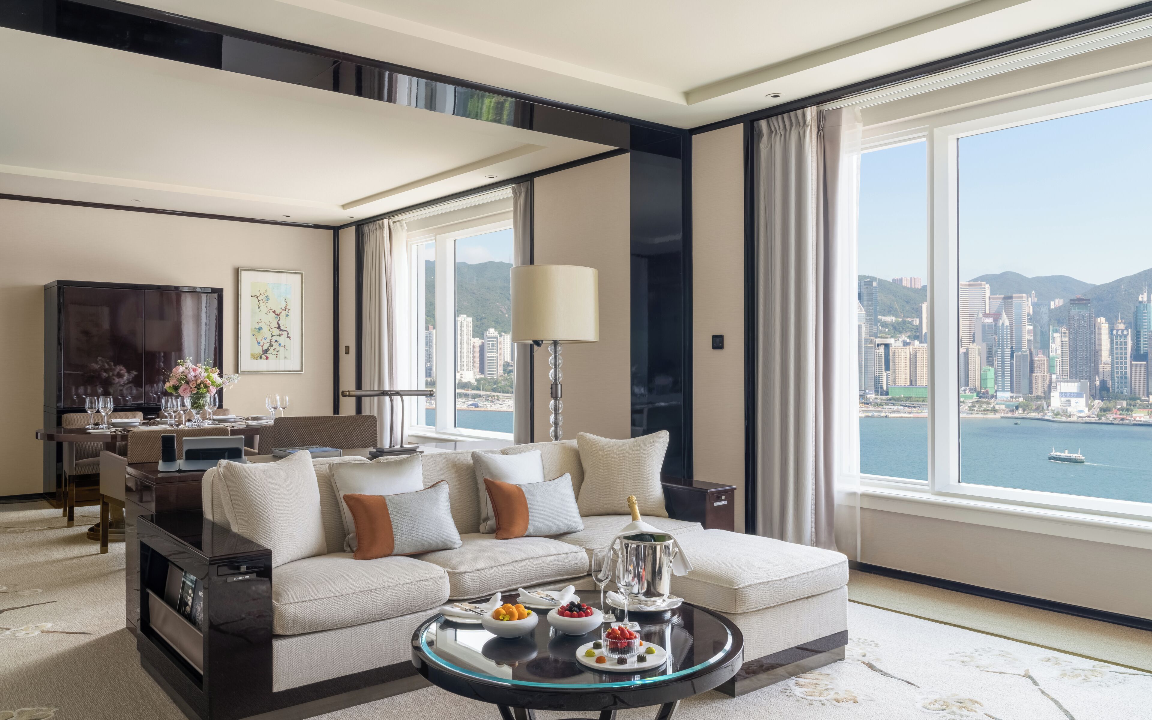 A modern living room with a sofa, a dining table, and a view of a cityscape through large windows.