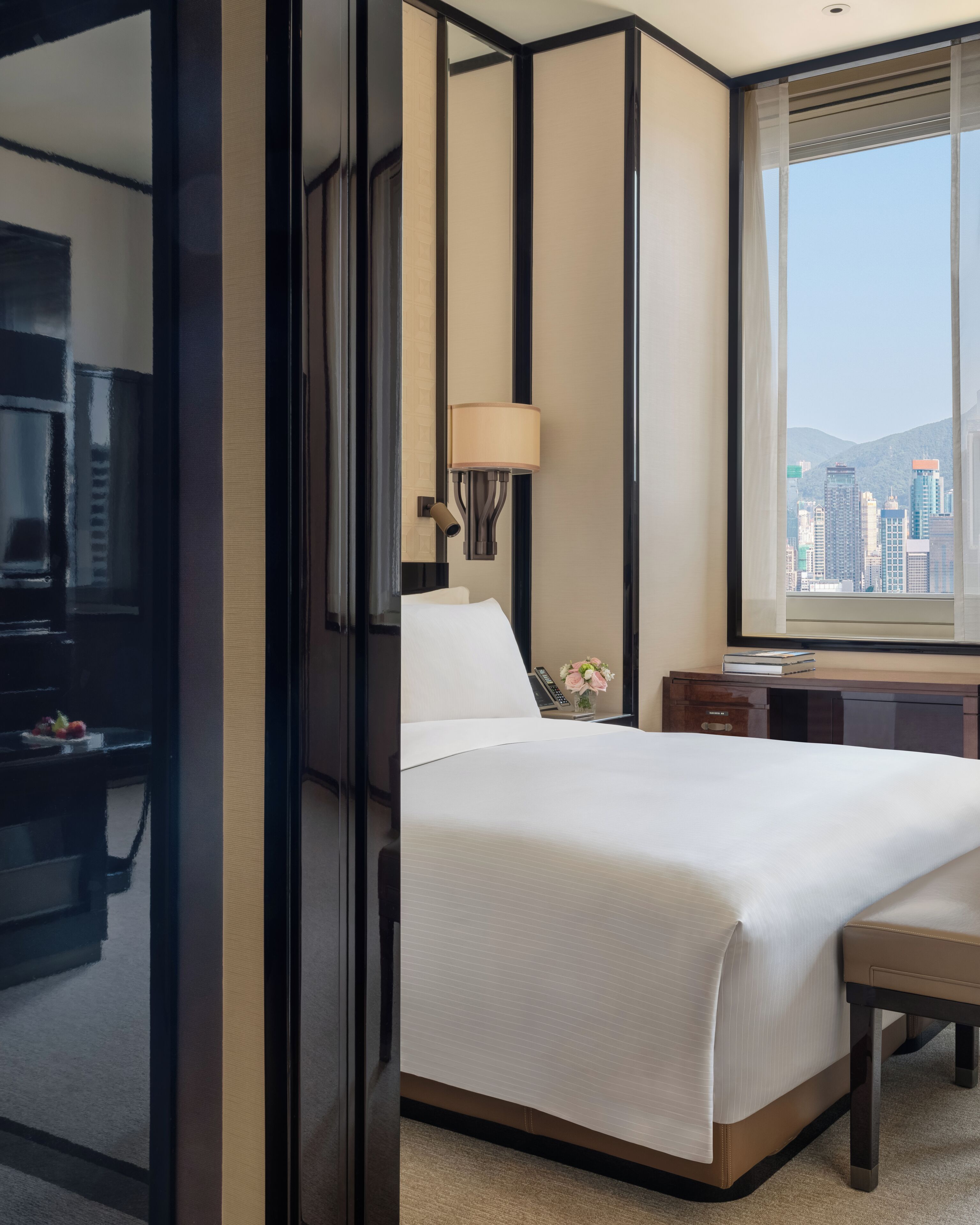 A hotel room with a bed, a desk, a lamp, a window with a city view, and a TV.