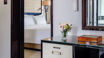 A hotel room with a bed, a desk with drawers, a mirror, and a vase with flowers.