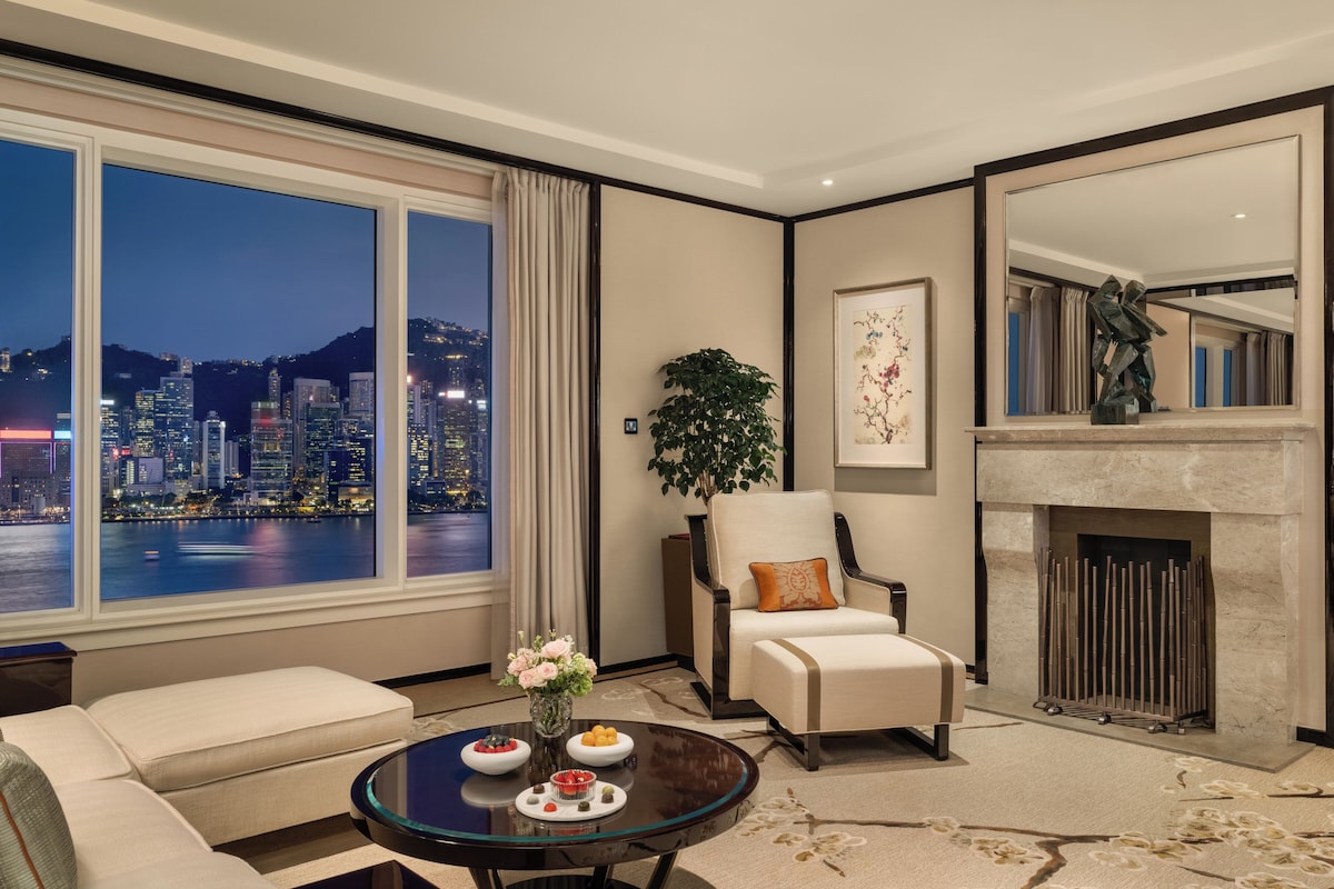 A modern living room with a large window overlooking a cityscape, a fireplace, and a seating area with a coffee table.