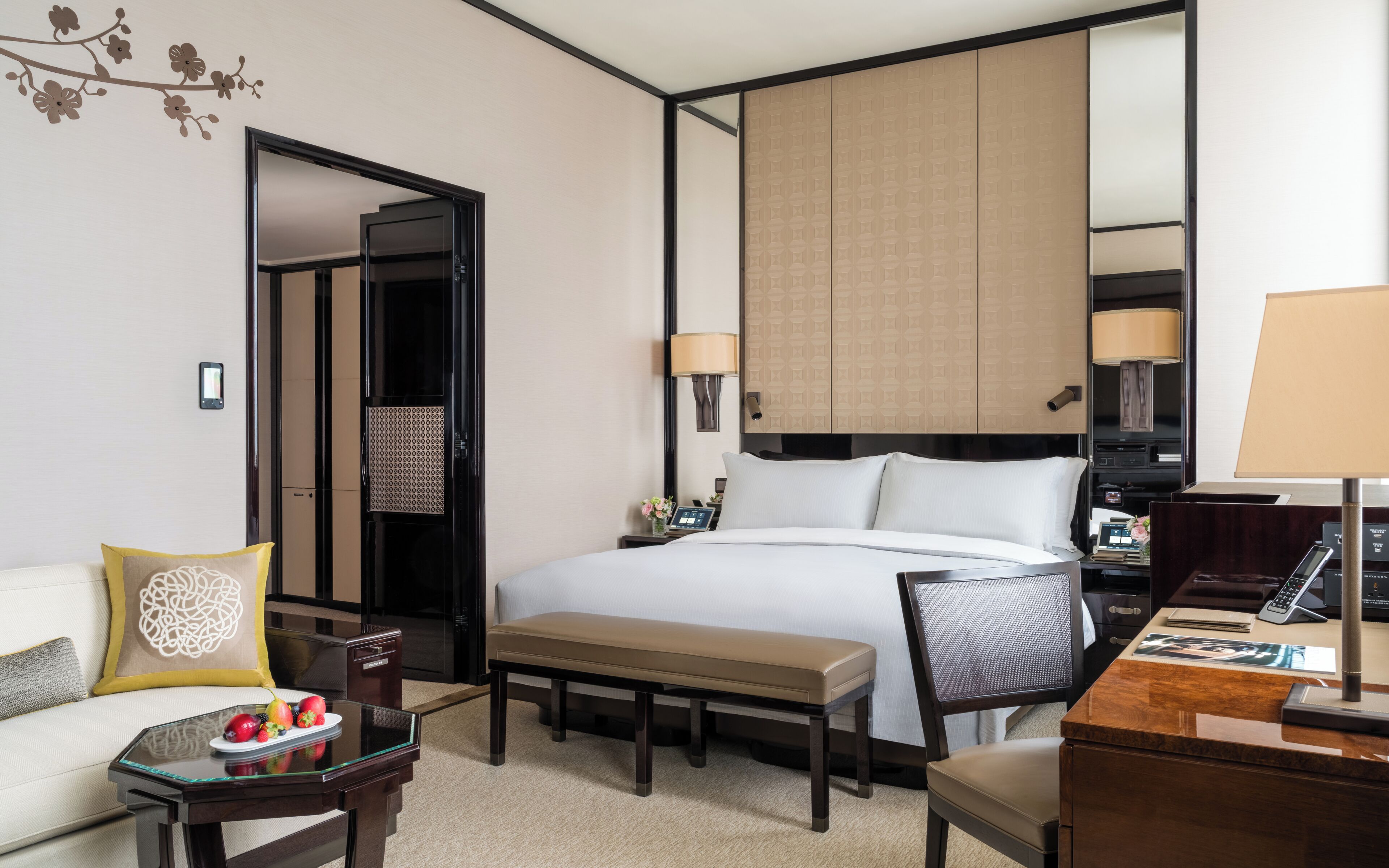 A hotel room with a bed, bedside table, lamp, chair, and a small table with fruit.