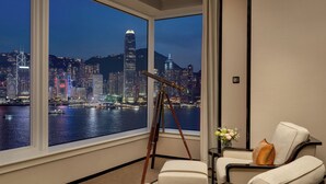 A hotel room with a large window overlooking a cityscape at night, featuring a telescope and seating area. - The Peninsula Hong Kong (Kowloon)
