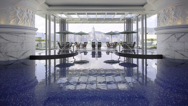 A luxurious indoor pool with marble columns, seating areas, and a city view. - The Peninsula Hong Kong (Kowloon)
