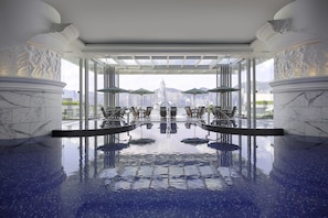 A luxurious indoor pool with marble columns, seating areas, and a city view. - The Peninsula Hong Kong (Kowloon)