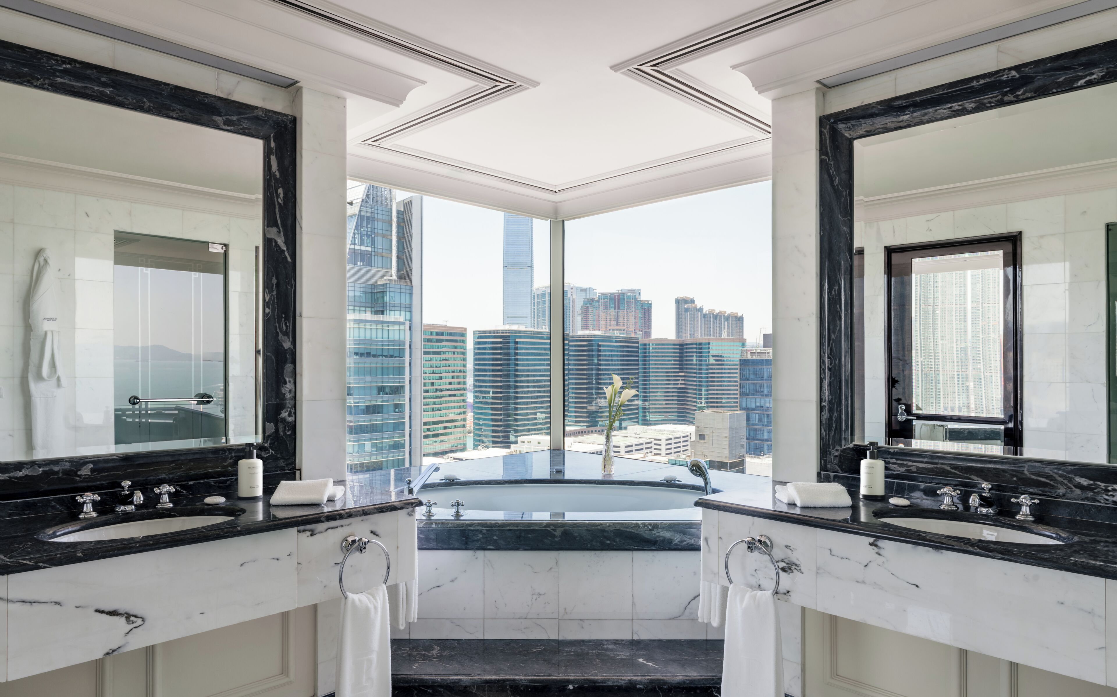 Une salle de bain moderne avec deux vasques en marbre, de grands miroirs et une vue sur la ville.