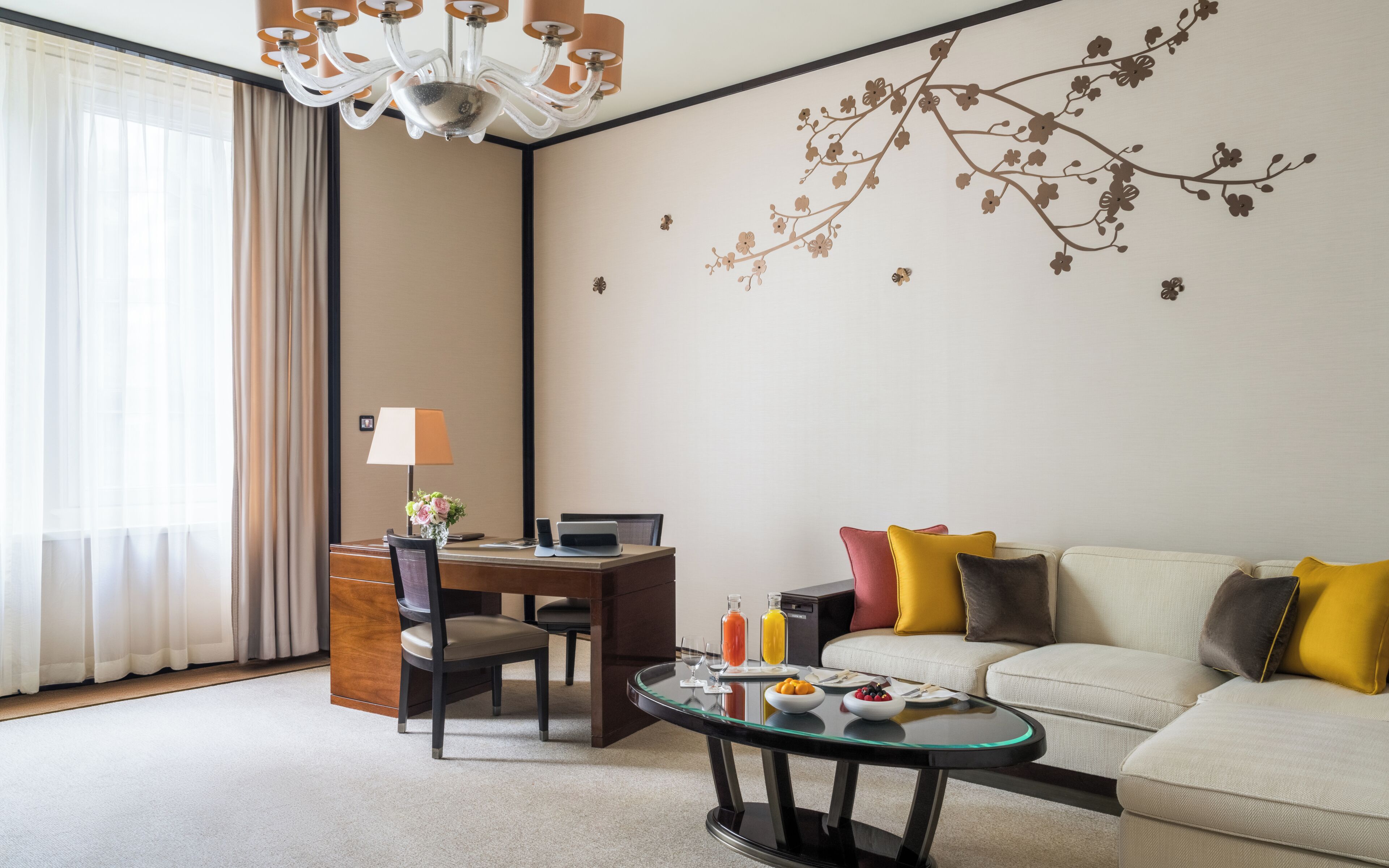 A hotel room with a dining table, a sofa, a glass coffee table, and a decorative wall mural.