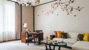 A hotel room with a dining table, a sofa, a glass coffee table, and a decorative wall mural.