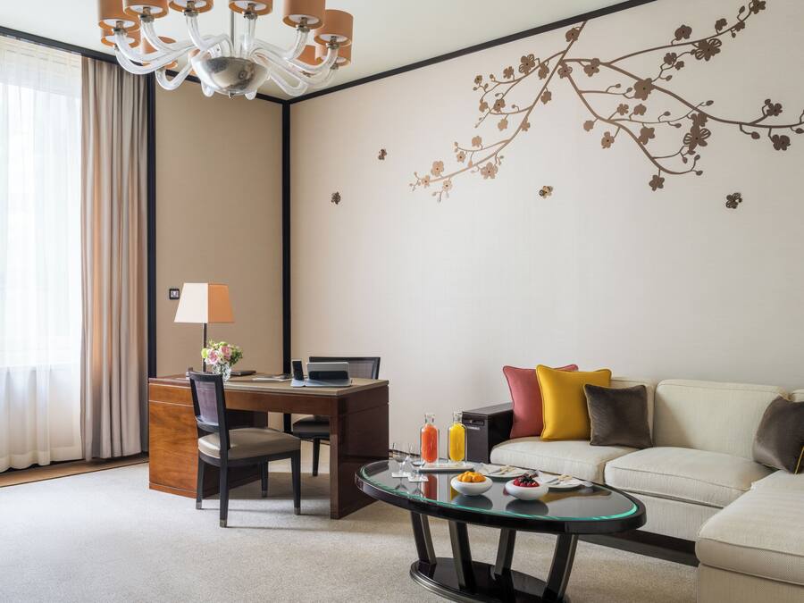 A hotel room with a dining table, a sofa, a glass coffee table, and a decorative wall mural.