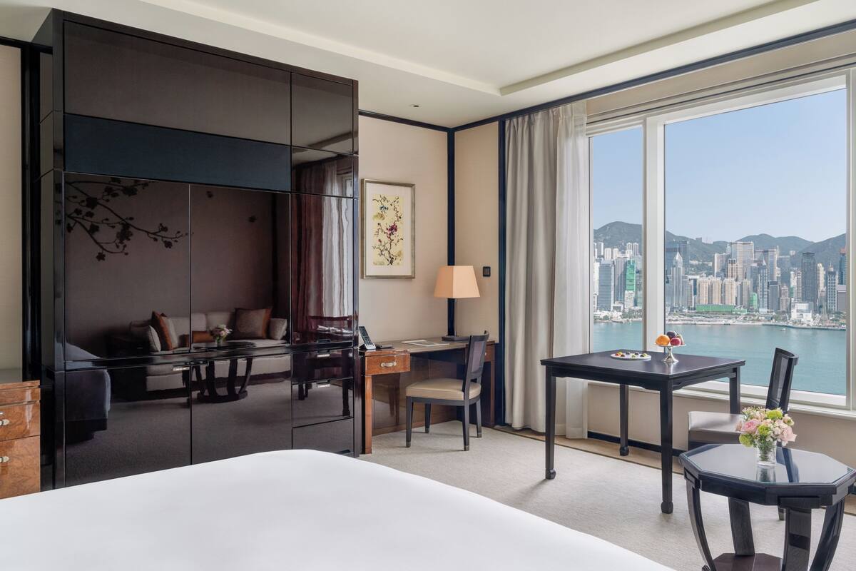 A hotel room with a bed, a desk, a chair, a sofa, and a view of a cityscape.