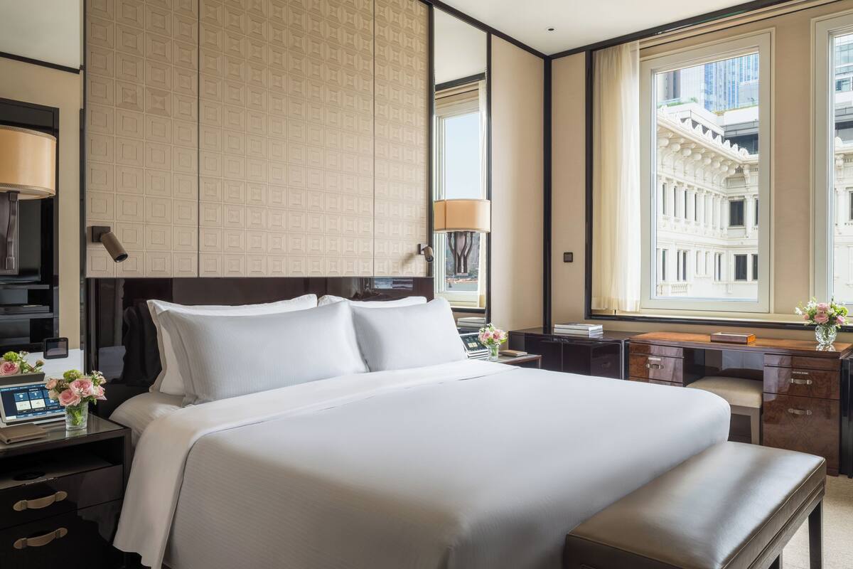 A hotel room with a large bed, a desk, a TV, and a window with a city view.