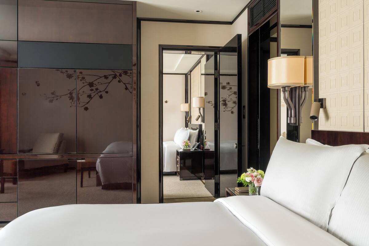 A hotel room with a bed, a desk, a chair, and a mirror.