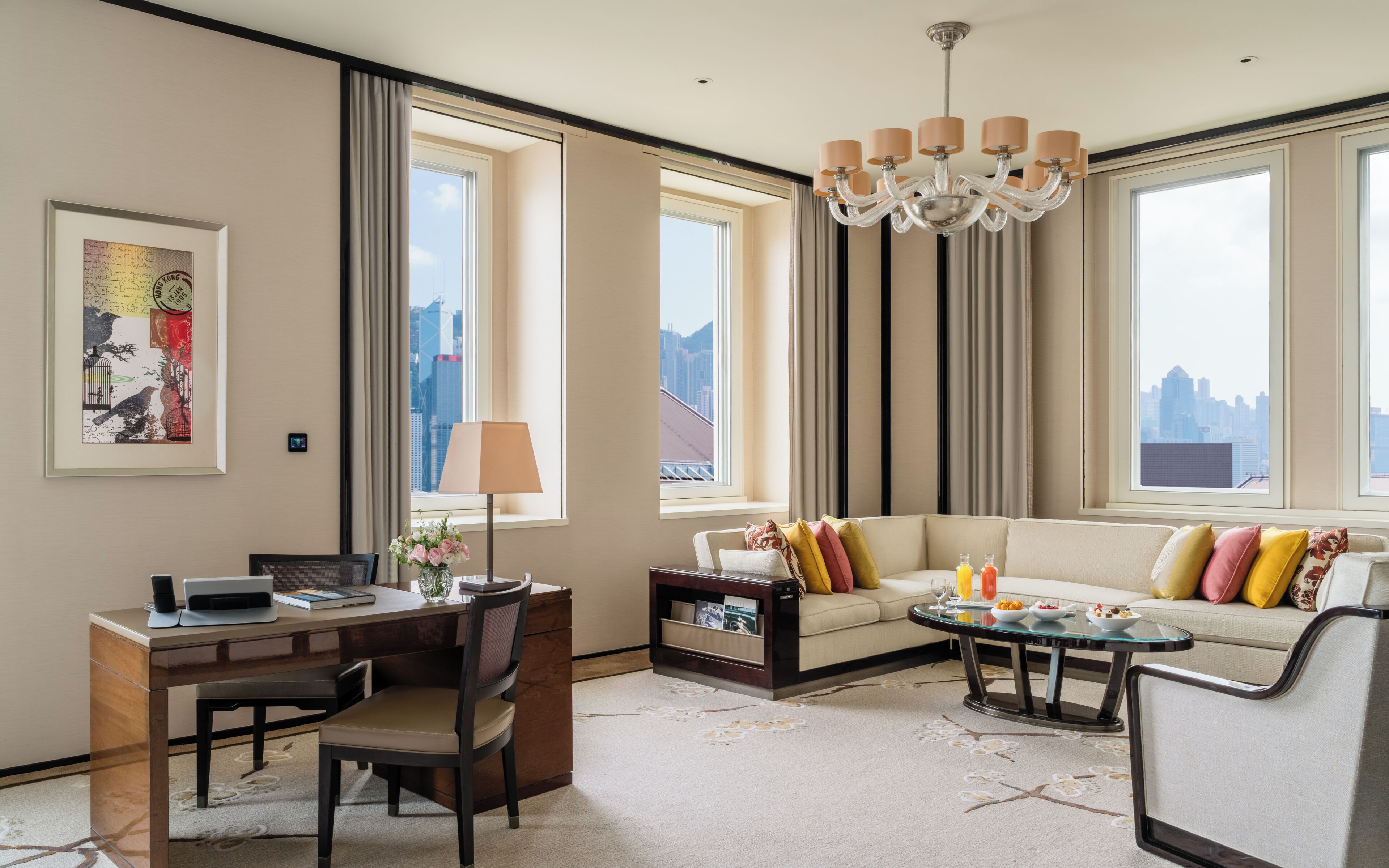 A modern hotel room with a sofa, dining table, and a city view.