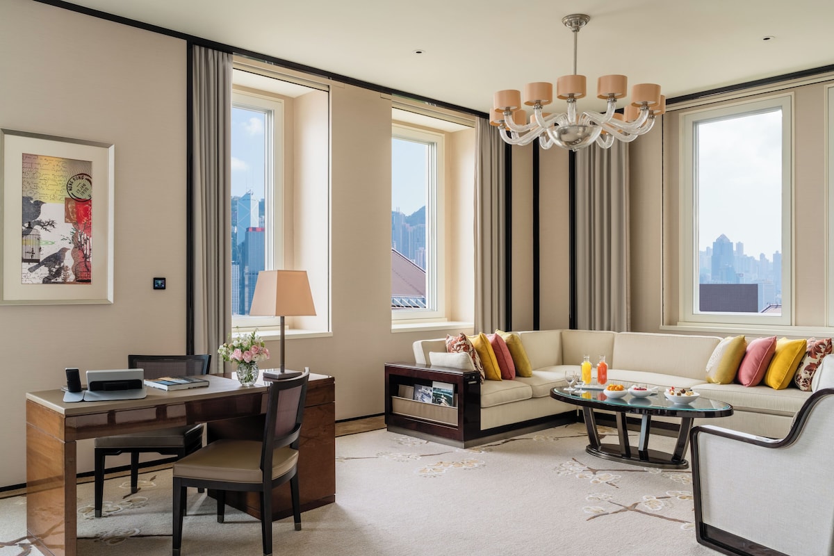 A modern hotel room with a sofa, dining table, and a city view.