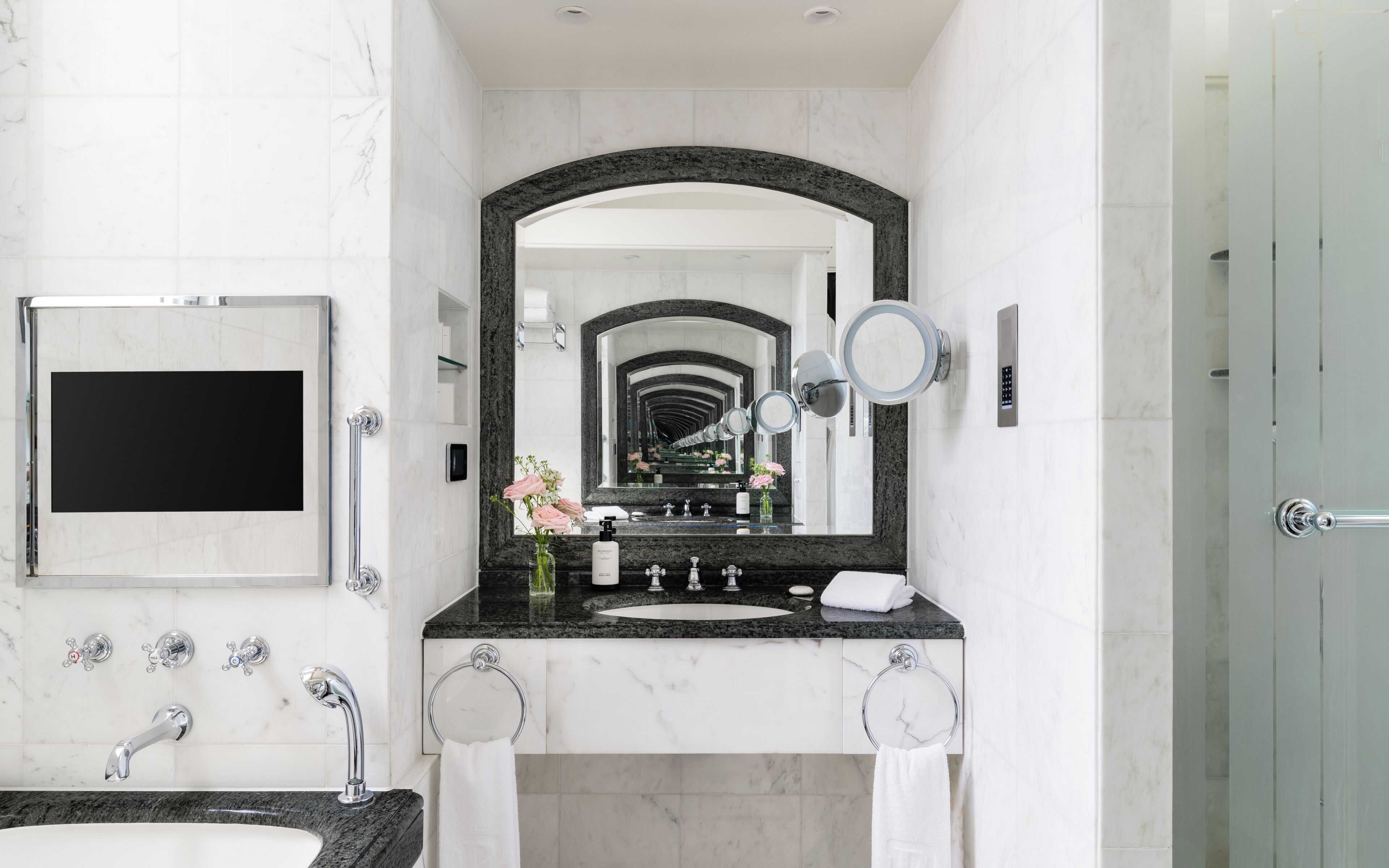 A modern bathroom with a large mirror, a sink, two faucets, a towel ring, and a glass shower door.