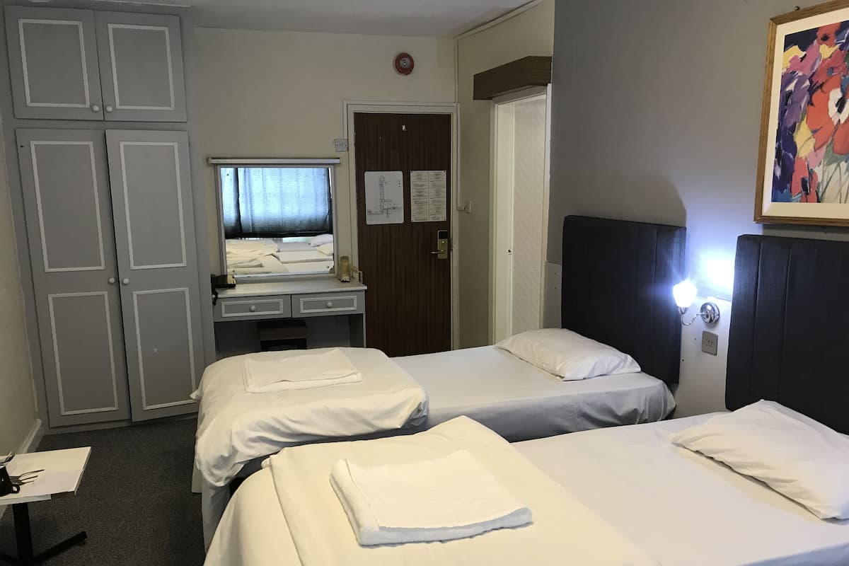 A hotel room with two beds, a desk with a mirror, a wardrobe, and a painting on the wall.
