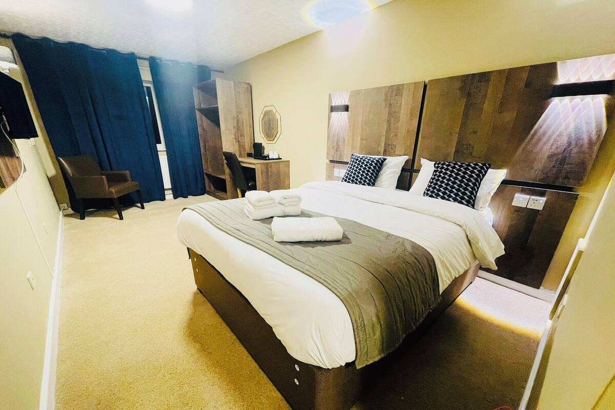 A hotel room with a large bed, a desk, a chair, and a mirror.