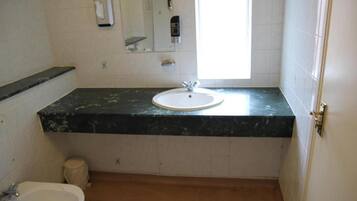 Un baño con lavamanos blanco, espejo, dispensador de toallas y ventana.